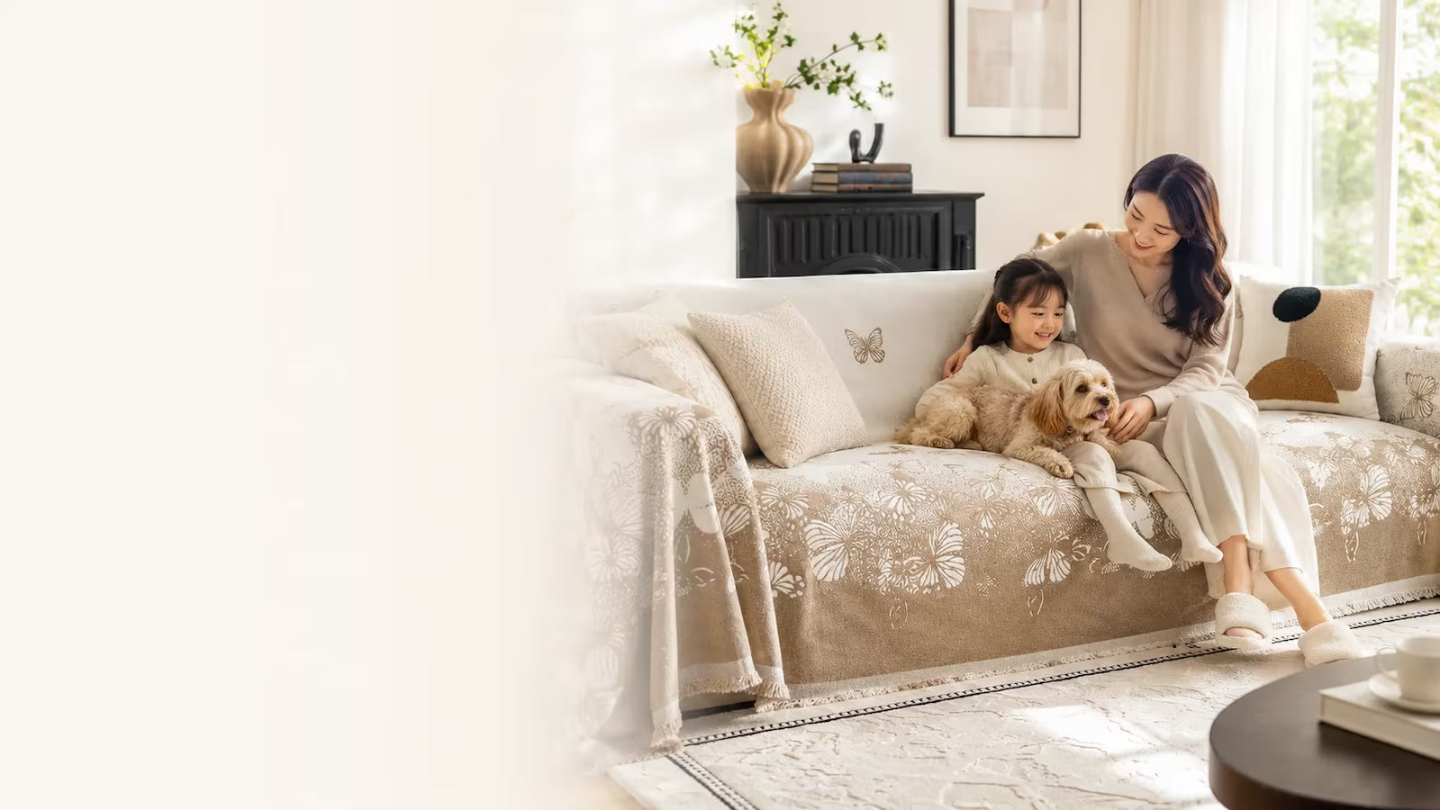 Woman and child sitting on a beige sofa with a dog, in a bright living room.